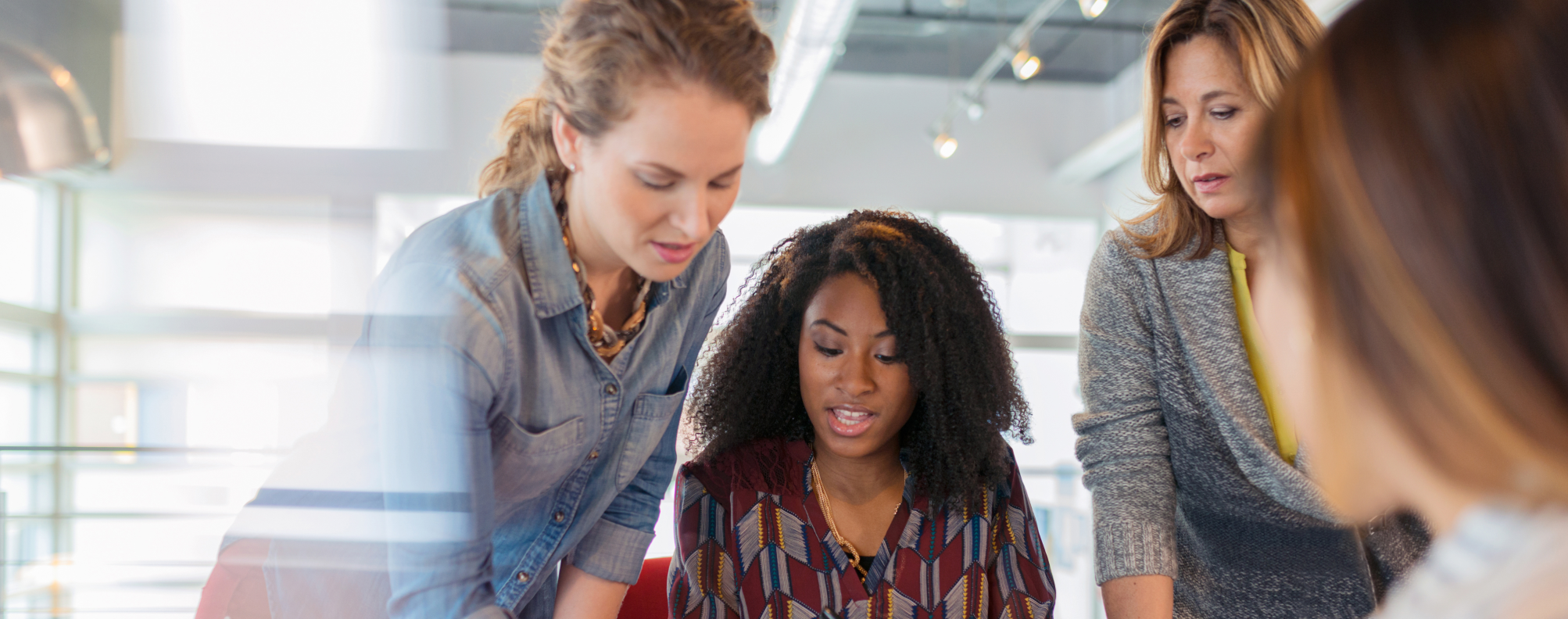 Four people in a conference room having a discussion as one writes on a sticky note.